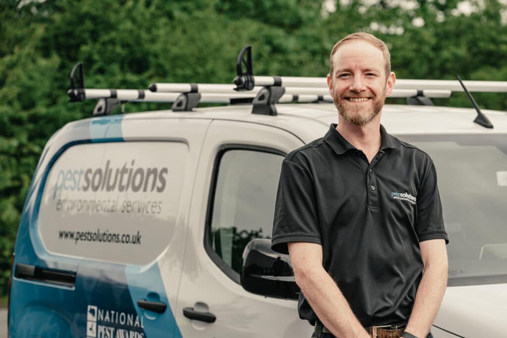 Standing in front of a company van is a Pest Solutions employee